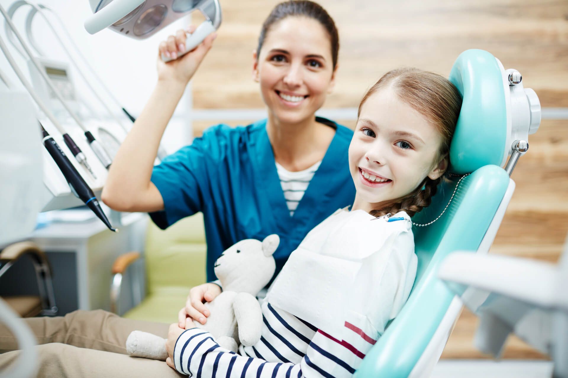 Little girl sitting in chair at dentist office with happy doctor near by