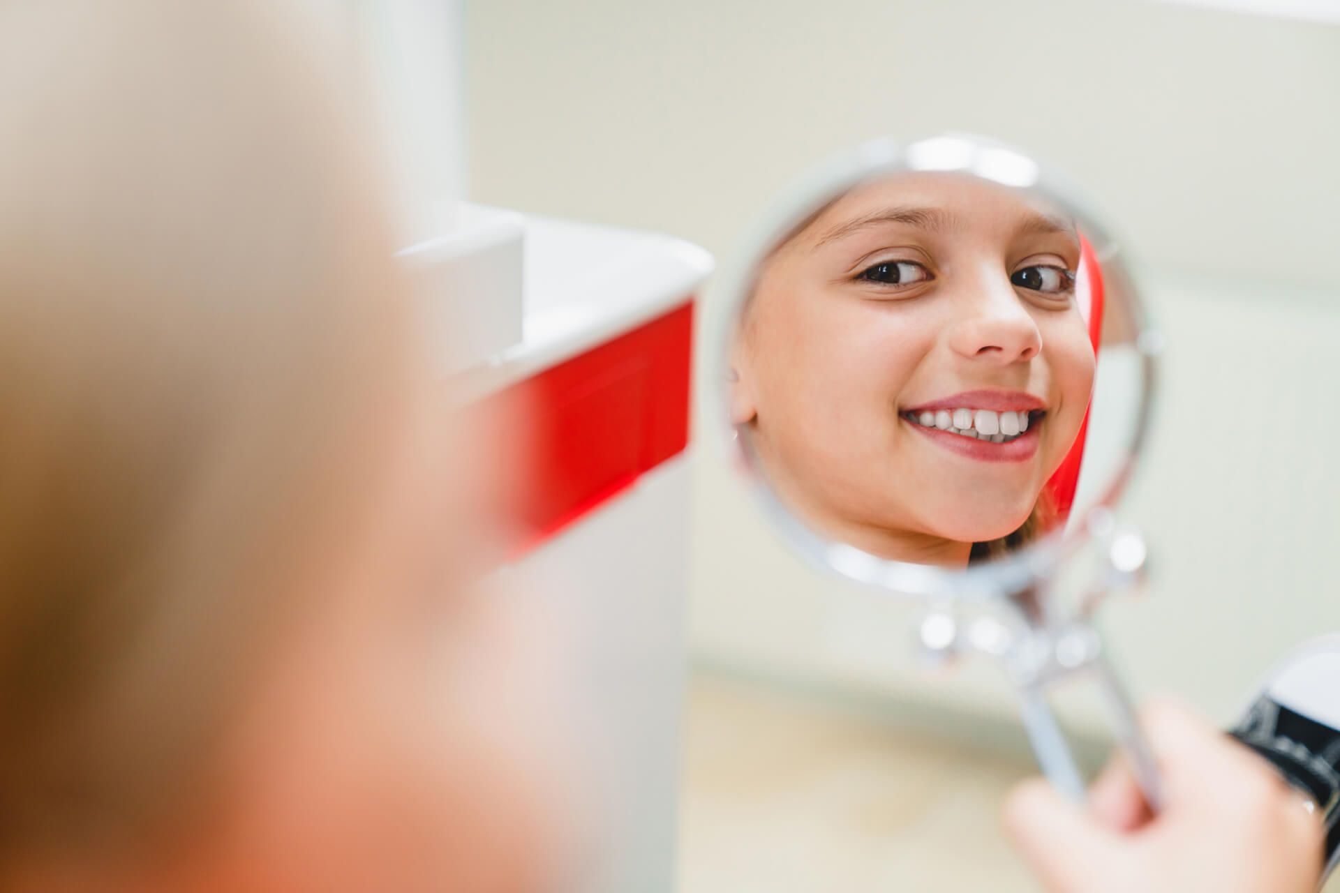 Small caucasian preteen girl looking at the mirror at dental clinic