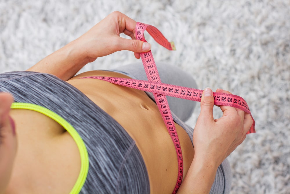 Slim Woman Measuring her thin waist with a tape measure.