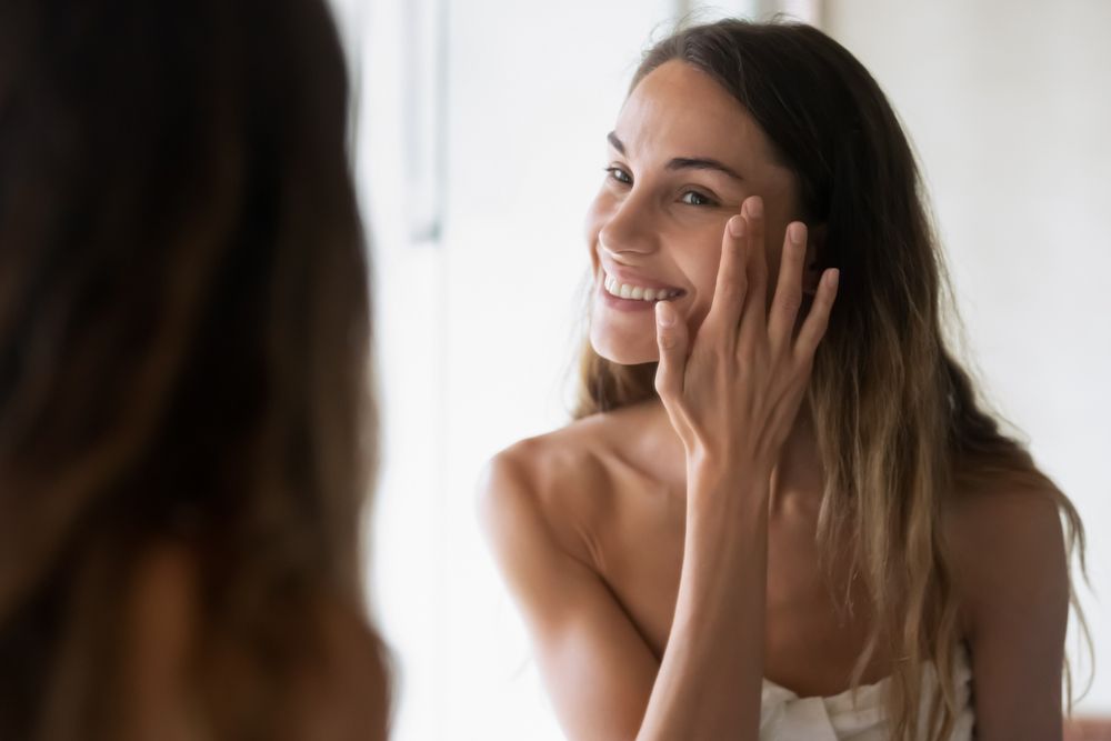 Woman smiling at her skin in the mirror after receiving PRP Therapy