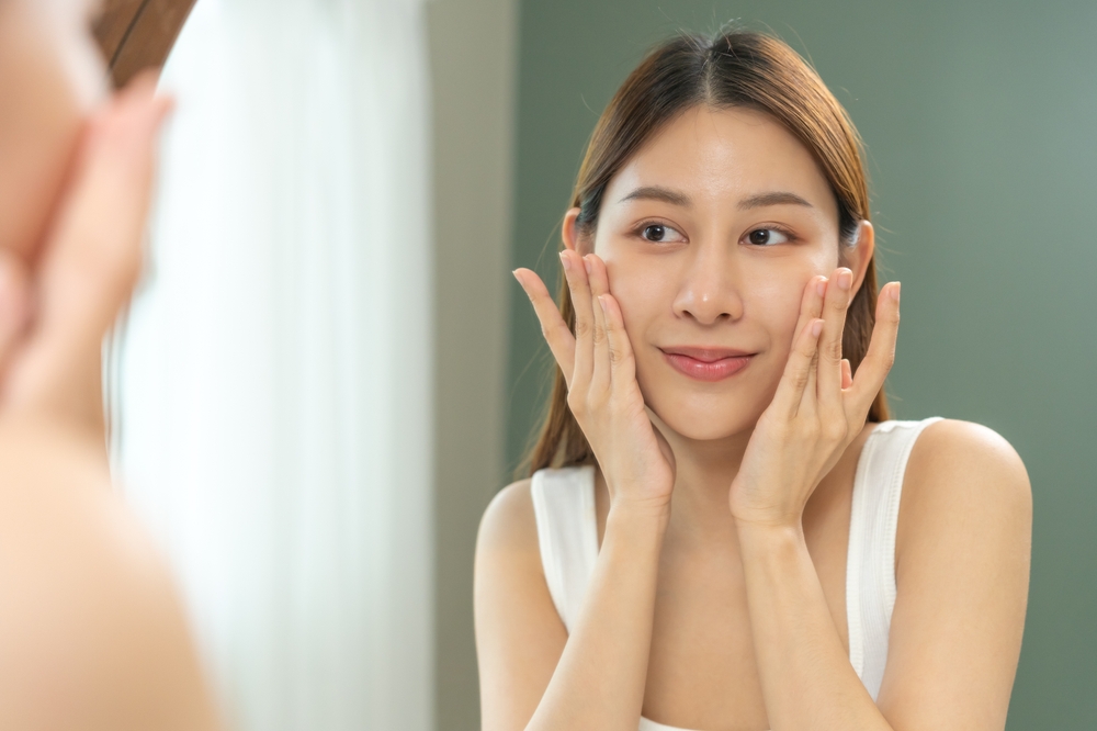 A woman smiling in the mirror after getting Dermal Fillers