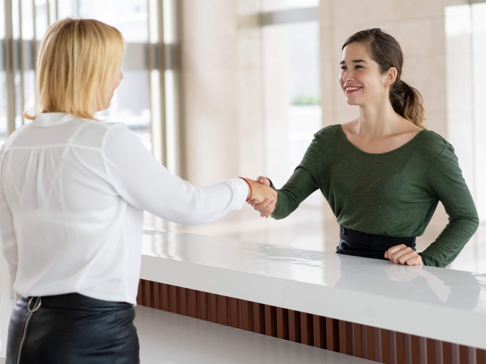 Office receptionist greeting corporate partner with handshake