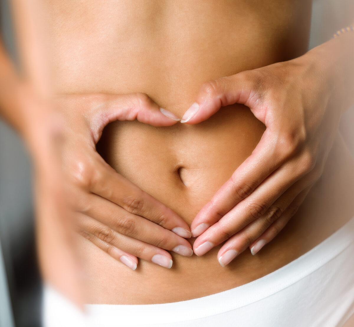 Beautiful woman making heart shape with her hands on her belly