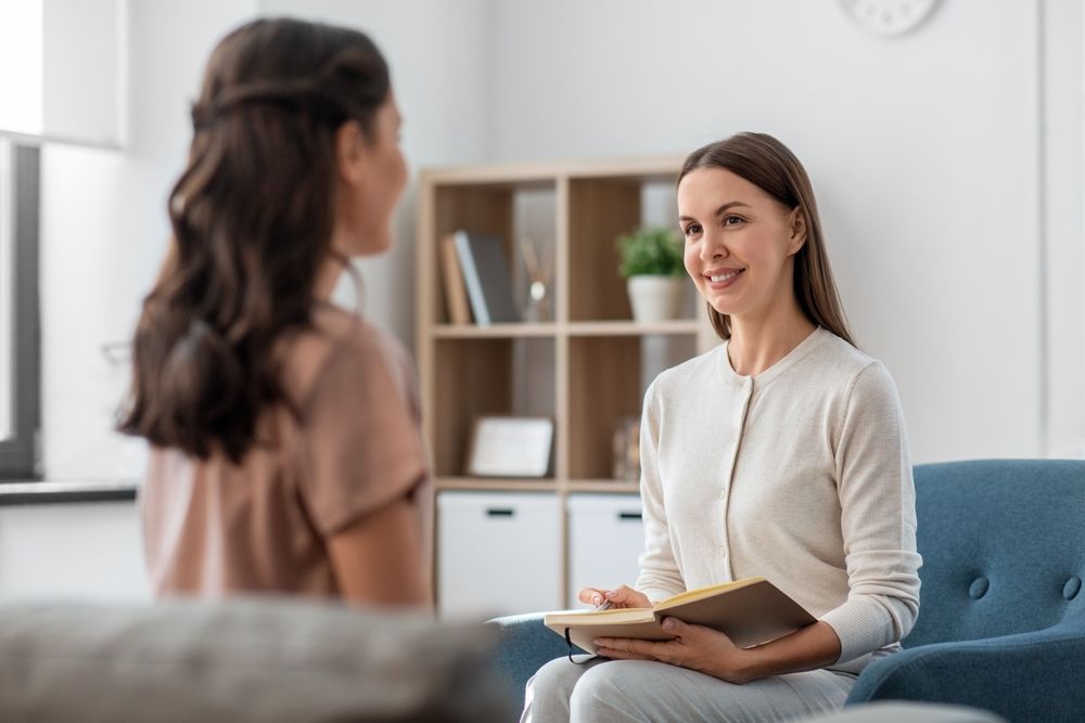 Smiling psychologist with notebook and woman patient at psychotherapy session
