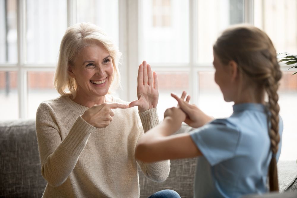 Smiling senior woman grandmother make sign language talk gesturing with granddaughter
