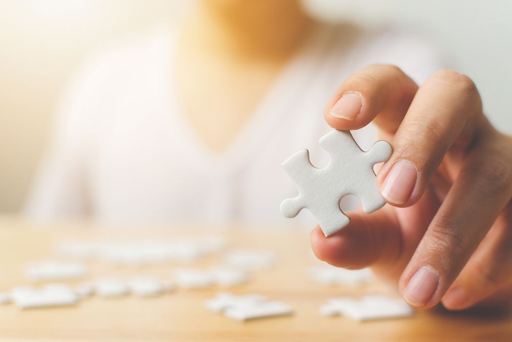 Hand of male trying to connect pieces of white jigsaw puzzle