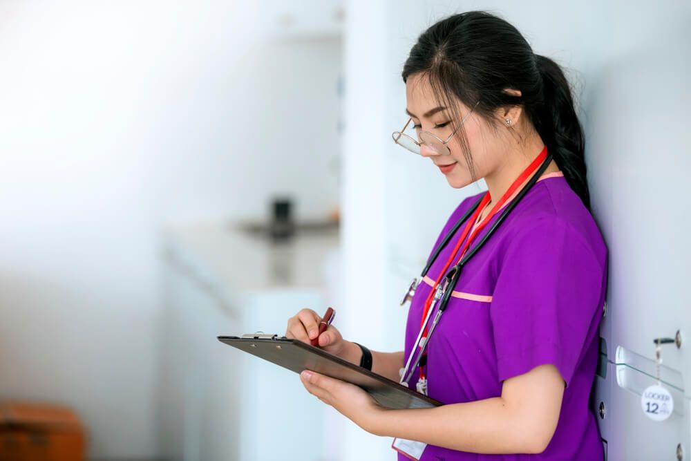 Nurse in purple uniform writing on medical chart