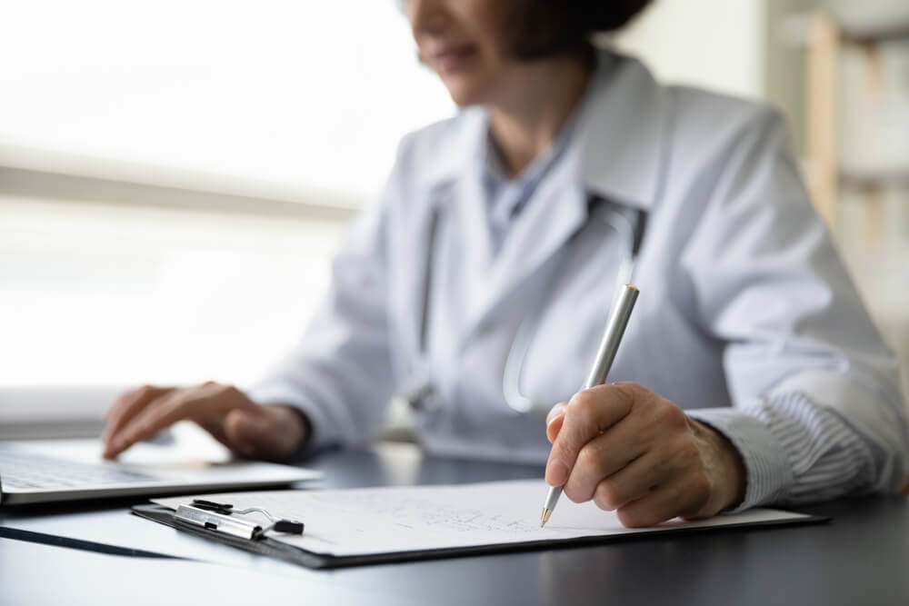 Hands of mature doctor woman filling paper medical records