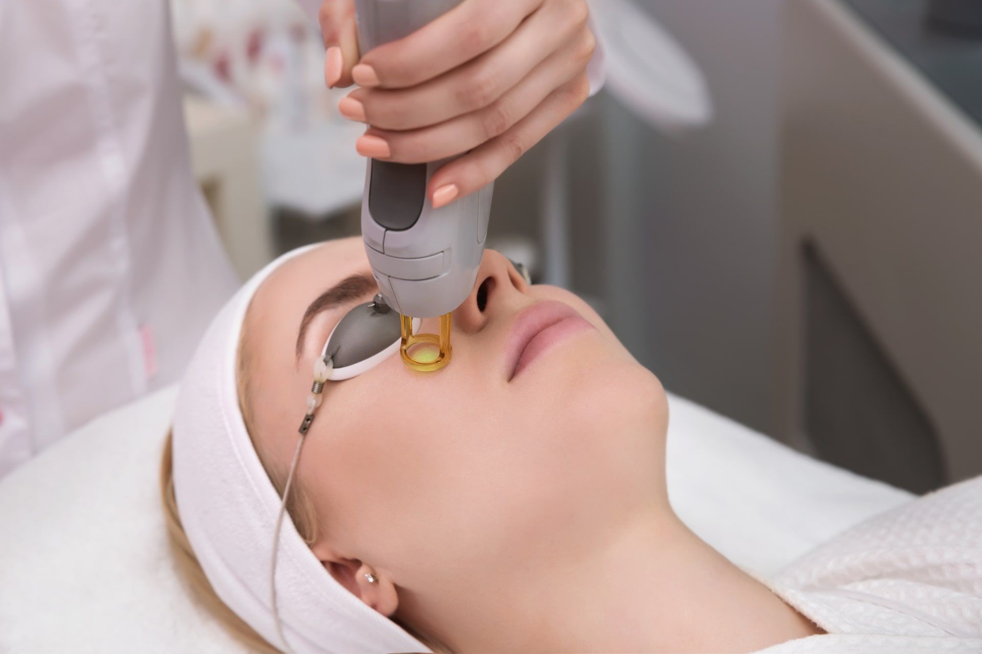 Therapist beautician makes a laser treatment to young woman's face