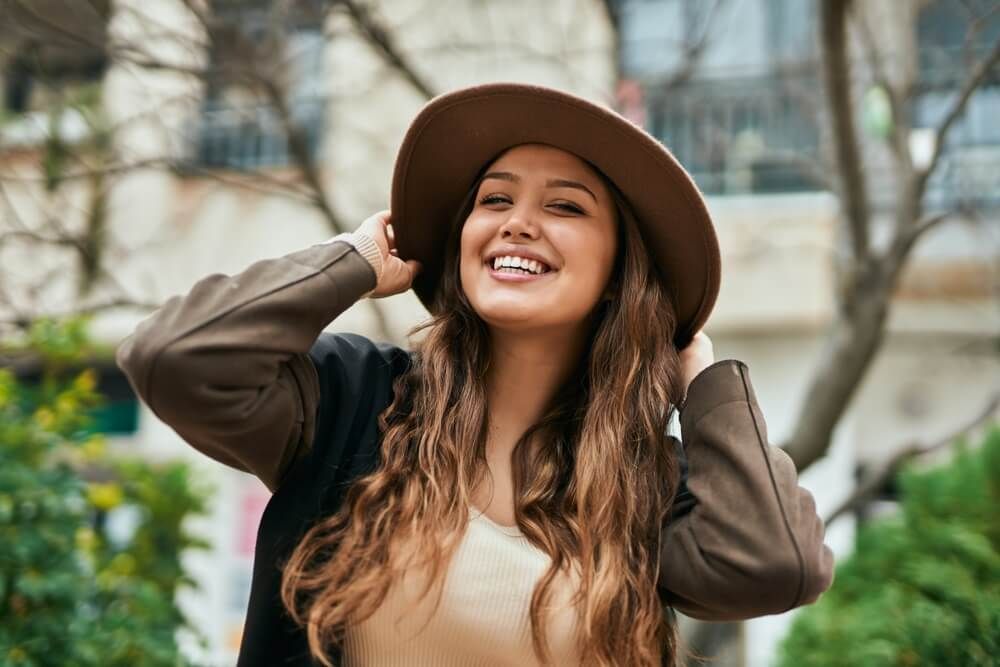 Young hispanic tourist woman smiling happy holding hat at the city.