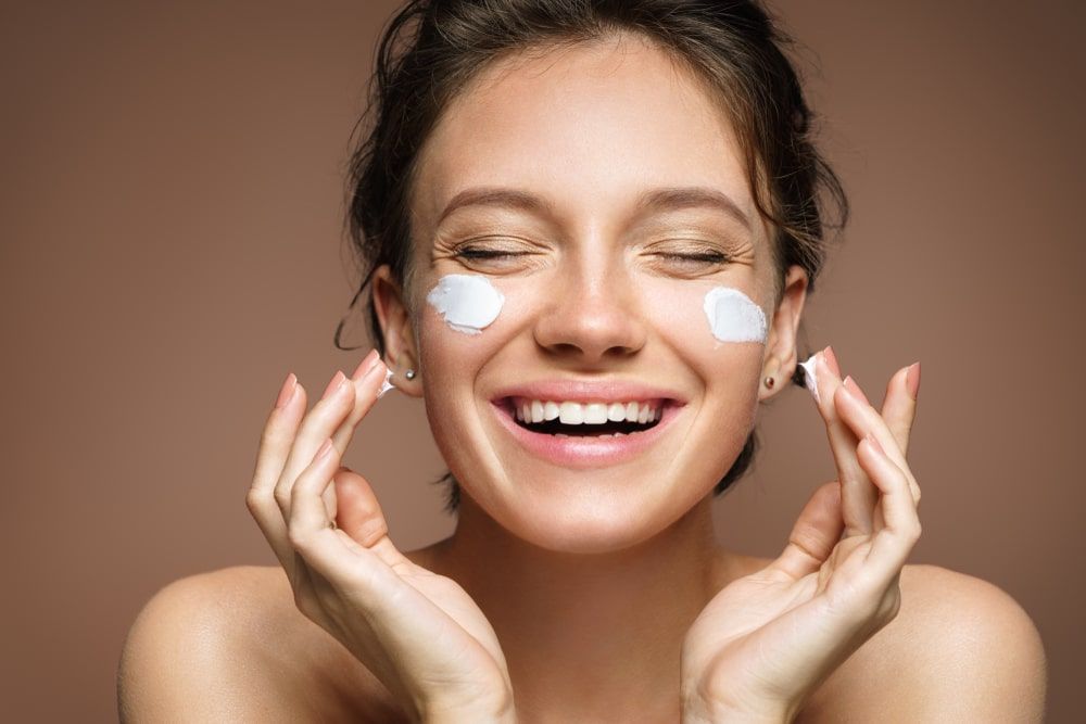 Laughing girl applying moisturizing cream on her face