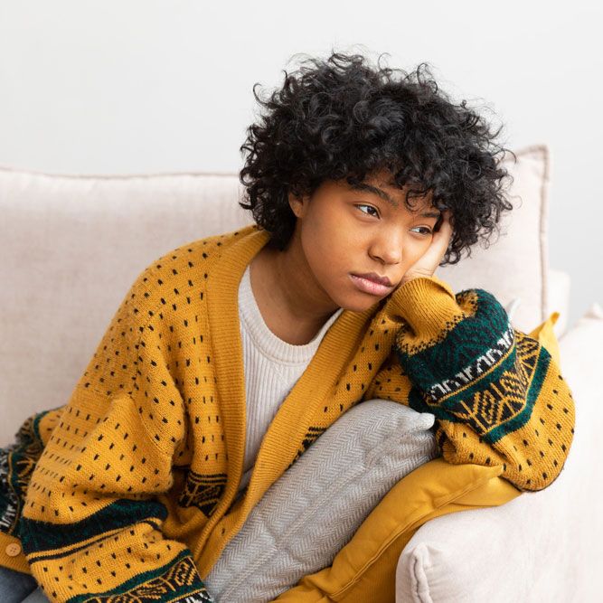 African american sad thoughtful pensive unmotivated girl sitting on sofa at home indoor.