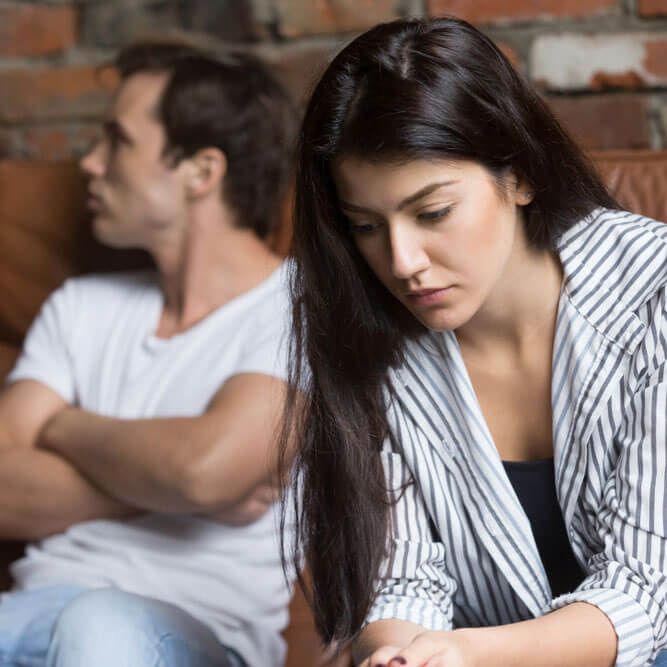 Sad pensive young girl thinking of relationships problems sitting on sofa with offended boyfriend