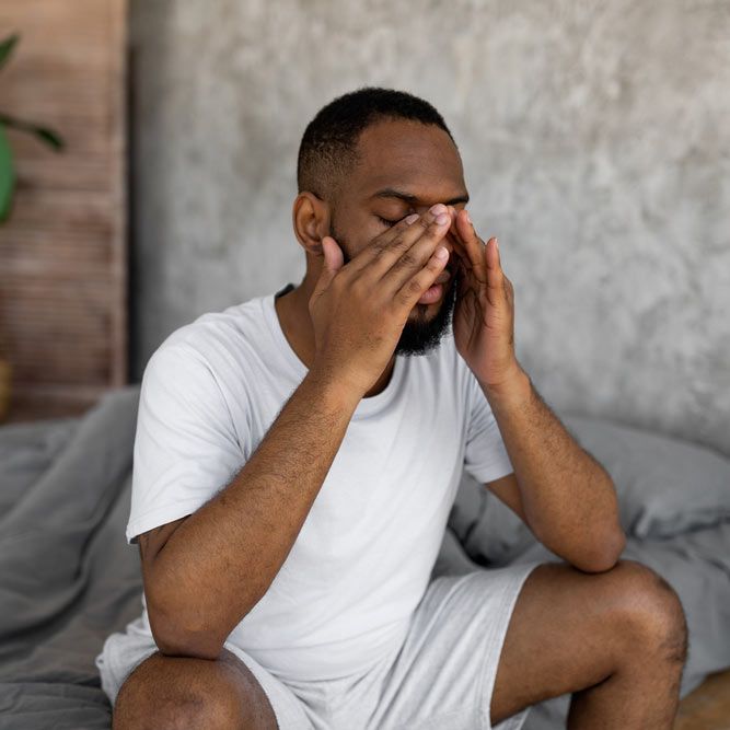 Young black man suffering from headache or migraine, rubbing eyes after waking up.