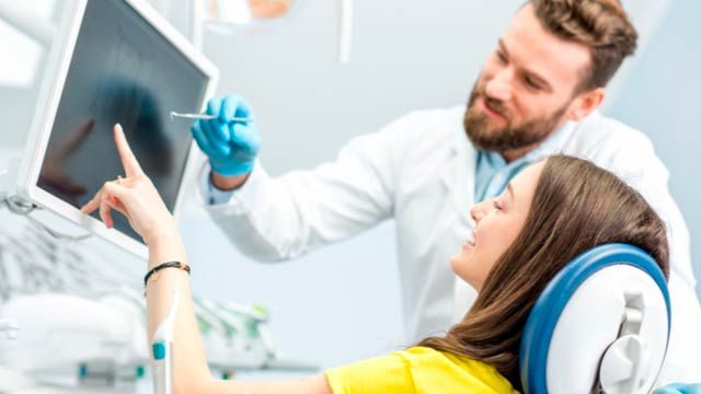 Photo of male dentist showing at patient's X-ray image in dental office.