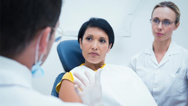 Portrait of smiling male dentist and assistant with female patient in the dentists chair