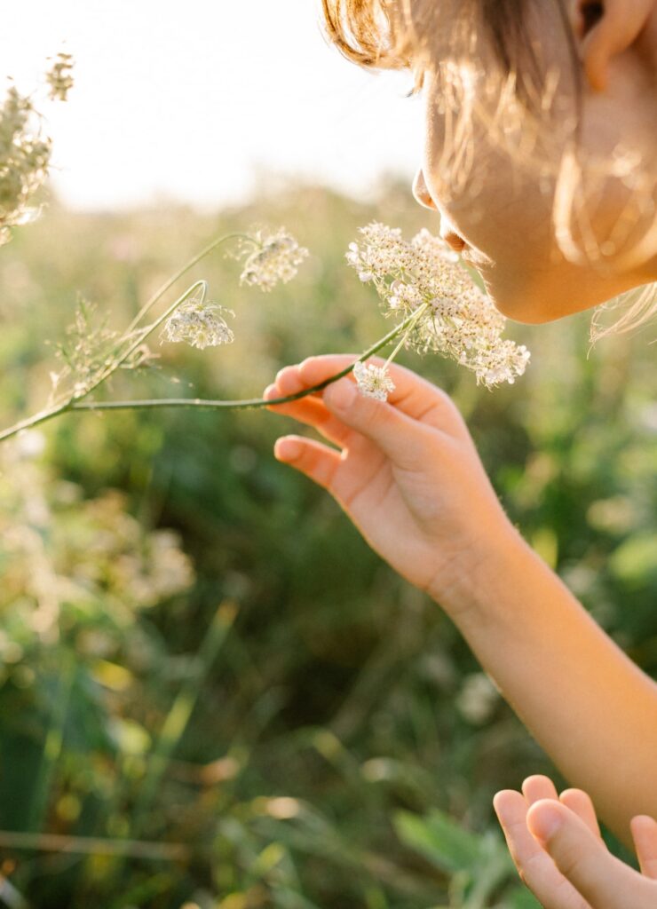 Little girl wearing natural white dress with wildflower motiv in green field with wild carrot flowers