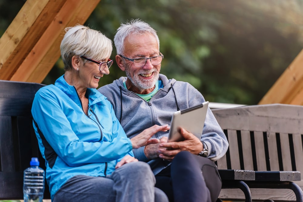 Smiling senior active couple sitting on the bench looking at tablet computer