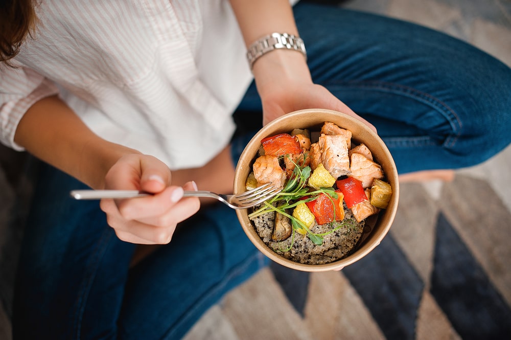 Girl holds a paper plate with healthy food sitting on the floor