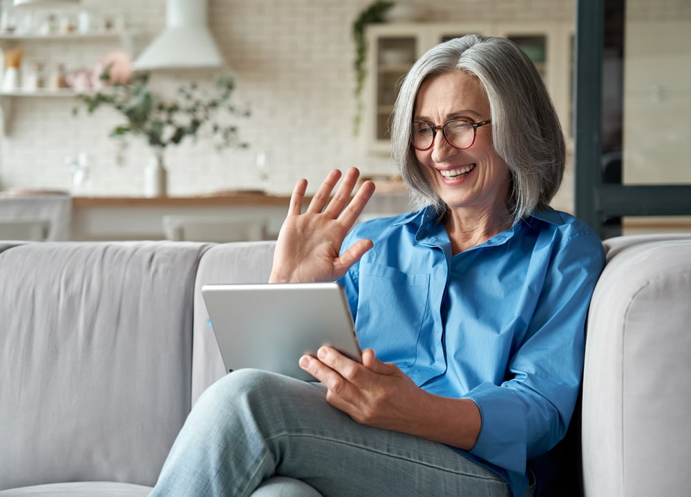 Happy 60s older mature middle aged adult woman waving hand holding digital tablet