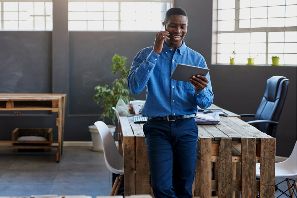 Smiling young man leaning on his desk in a large modern office