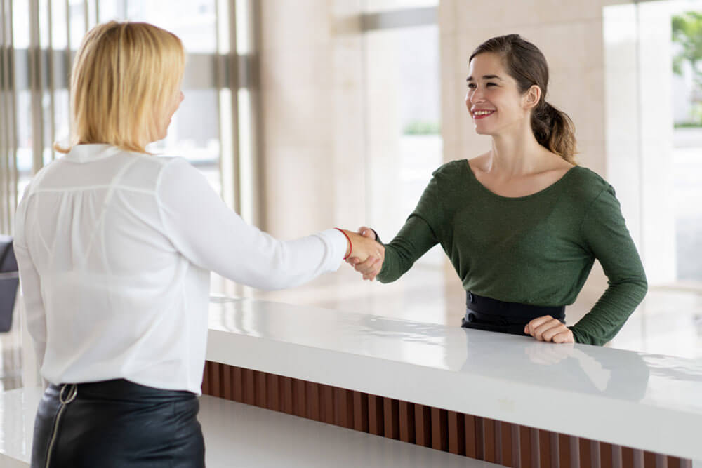 Office receptionist greeting corporate partner with handshake