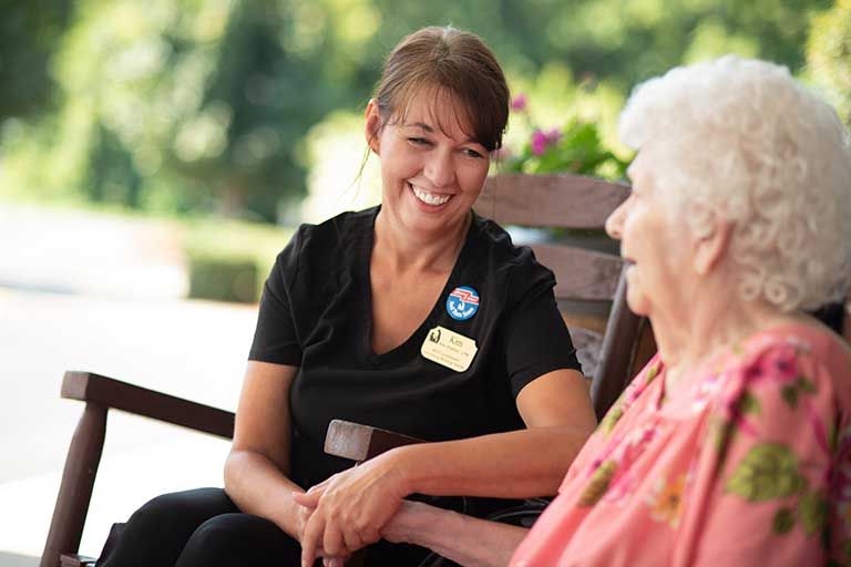 Senior Woman Sitting In Chair And Talking With Nurse