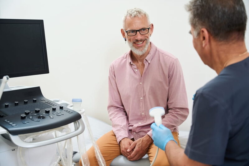 Gray-haired man in an ultrasound room communicates with a doctor