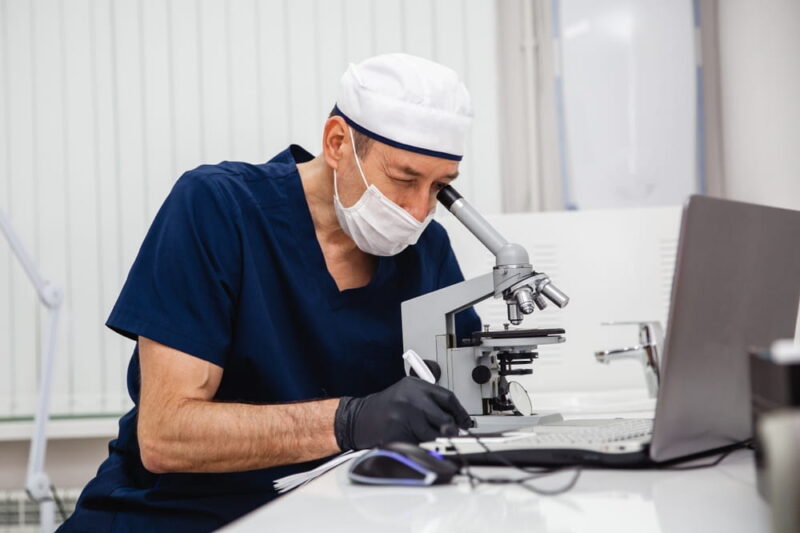 male doctor is looking into microscope for biopsy