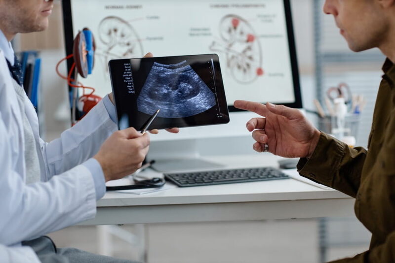 Middle aged Caucasian male urologist showing ultrasound scan on digital tablet to man during medical consultation in clinical office,