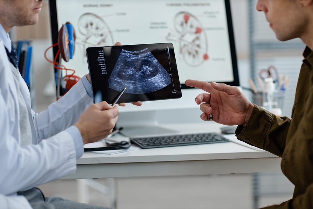 Middle aged Caucasian male urologist showing ultrasound scan on digital tablet to man during medical consultation in clinical office,