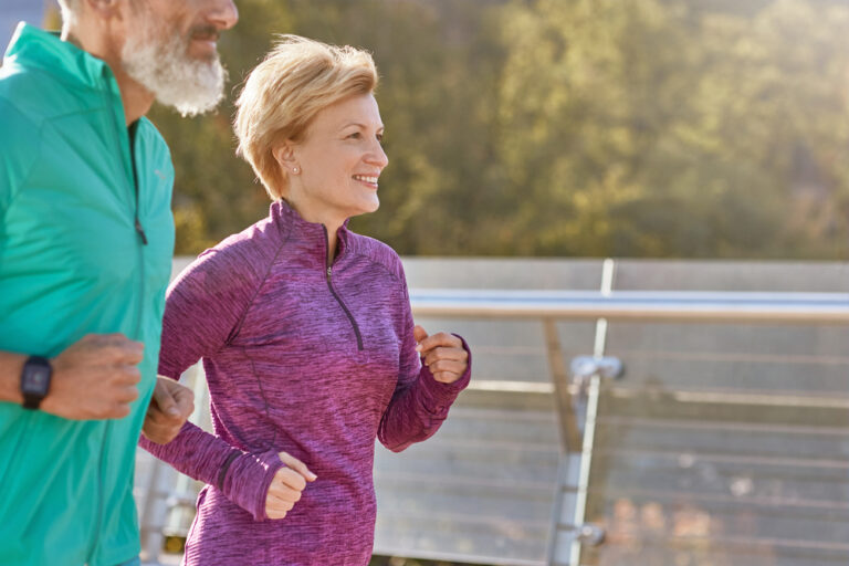 Cheerful active mature woman in sportswear smiling while running on a sunny day