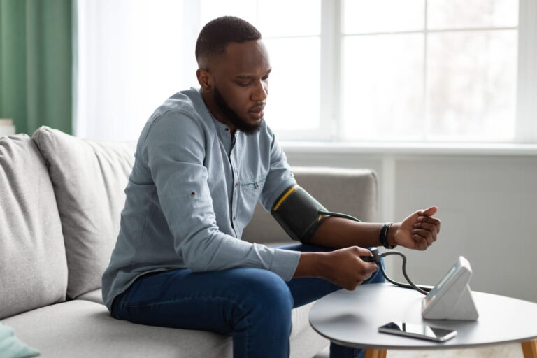 Hypertension Problem. Black Young Man Measuring Arterial Pressure Feeling Bad Sitting On Couch At Home