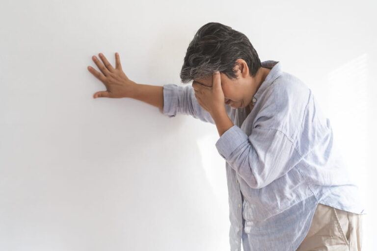 Dizzy asian elderly woman headache or migraine pain. suffering from vertigo, old standing up leaning on wall at home,
