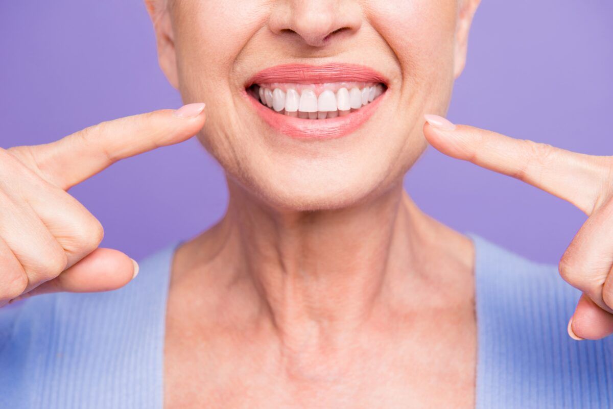 senior woman pointing to perfect teeth