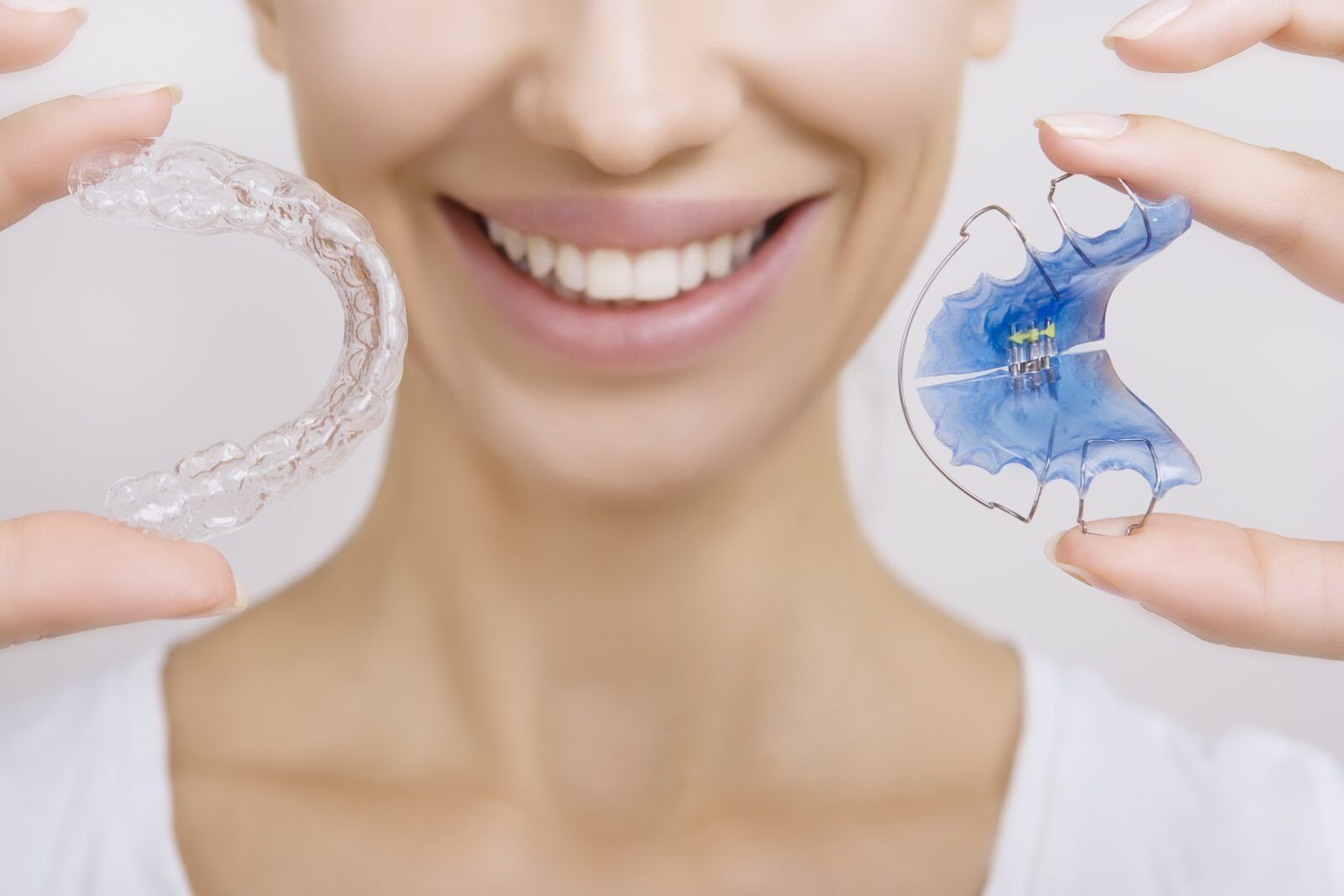 woman holding clear orthodontic aligner and hawley retainer