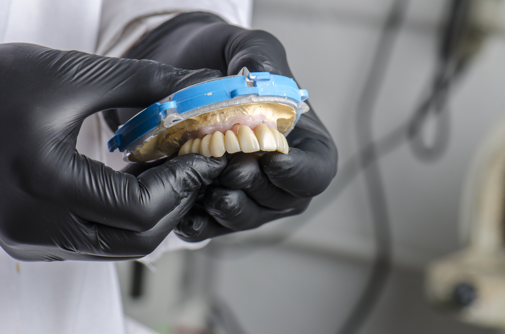Dental technician holding a monolithic zirconia restorations full arch implant supported with the ceramic load in vestibular