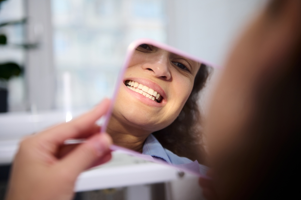 Close-up reflection in the cosmetic mirror of a pretty woman, female patient sitting in dental chair,