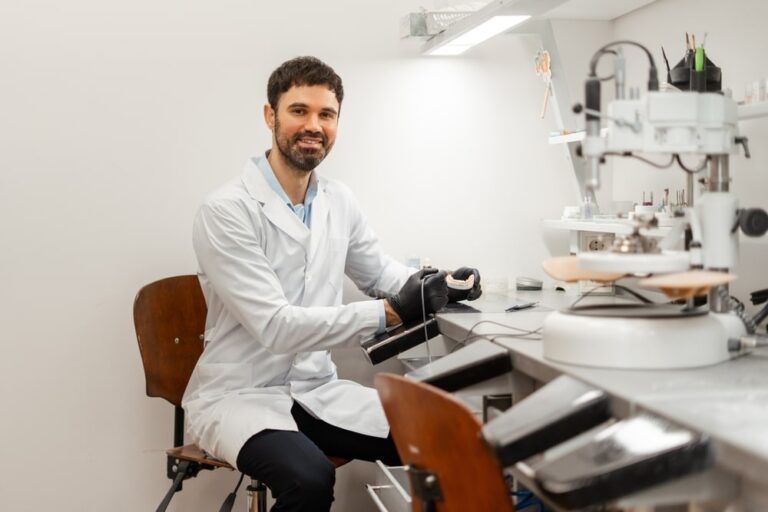 Smiling dental technician wearing black gloves working on a denture in a dental laboratory using specialized equipment and tools
