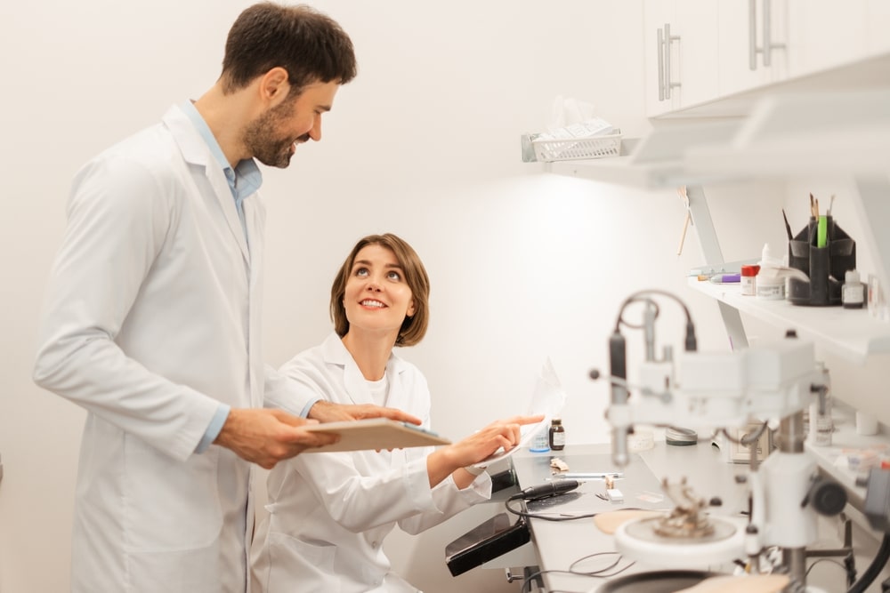 Two smiling dental technicians are discussing and analyzing information from a digital tablet and documents