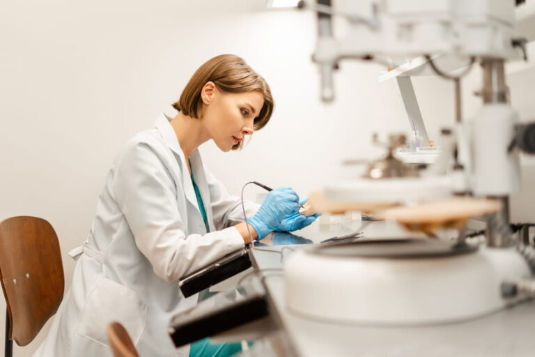 Female dental technician is working on a dental prosthesis with an electric milling machine in a dental laboratory, performing precision work for dental implants