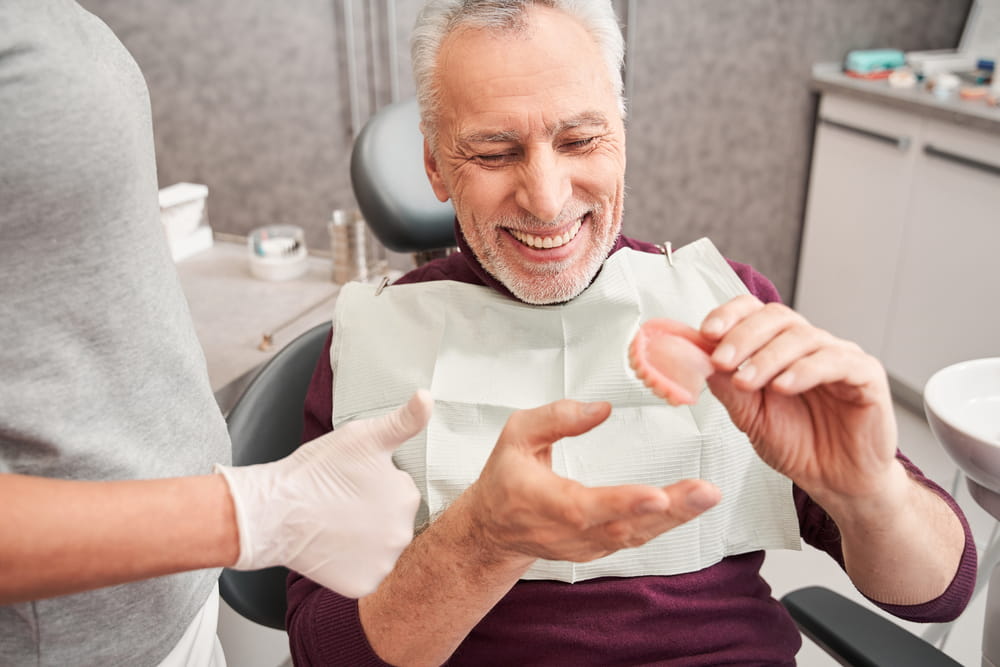 My new teeth. Cropped view of the dentist showing to senior grey haired patient teeth dentures while working at the dental clinic.