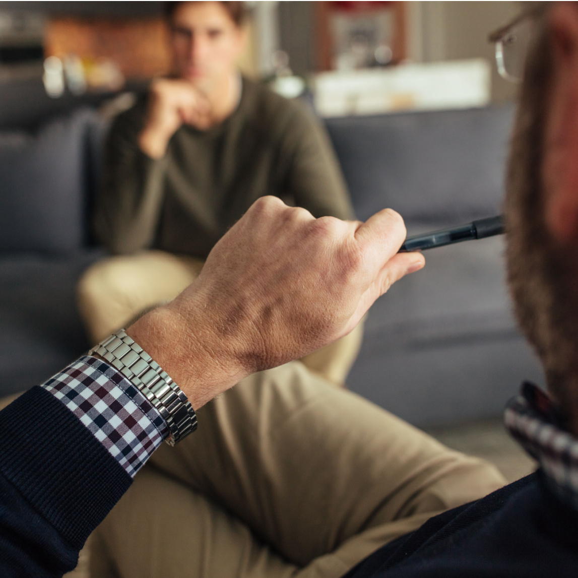 Hands of psychologist holding a pen and listening to man during therapy session