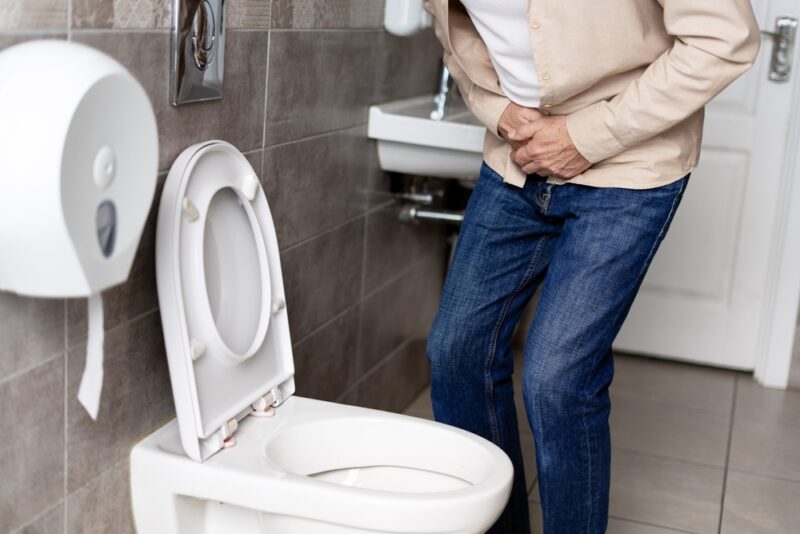 Elderly man experiencing discomfort from stomach or bladder pain while using a public toilet, highlighting issues related to aging and health