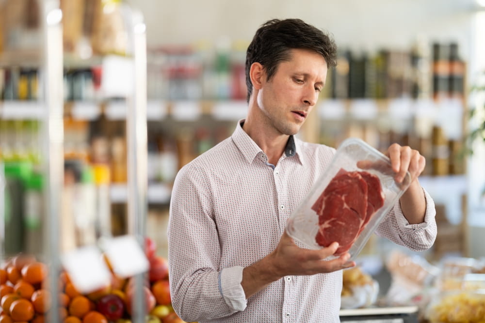 Adult man buyer chooses packaged raw beef entrecote in grocery store