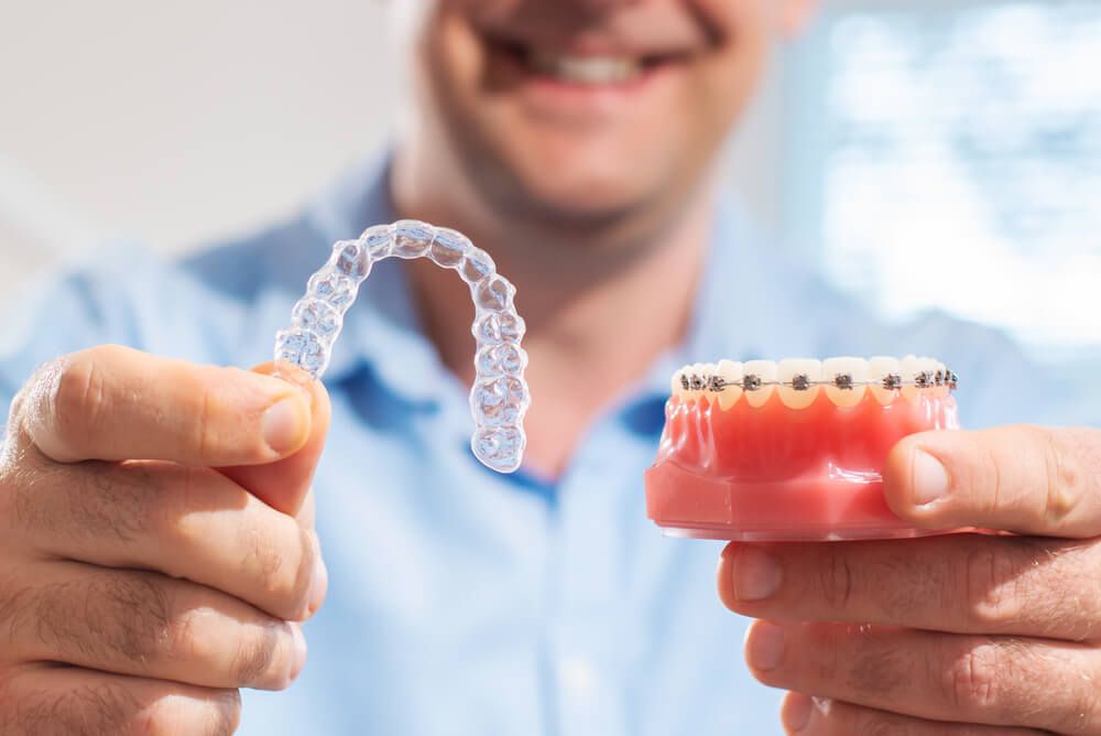 Smiling dentist doctor holding aligners and braces