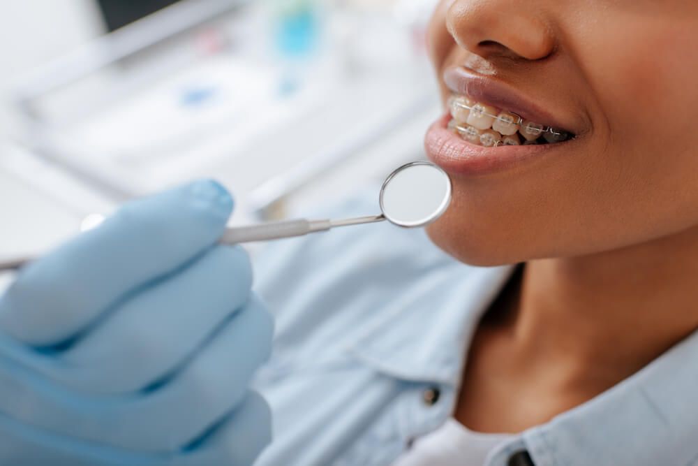 orthodontist holding dental mirror near happy patient in braces