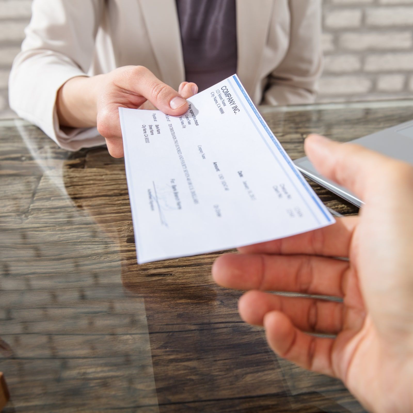 Close-up Of A Business Woman Giving Cheque To Her Colleague At Workplace In Office