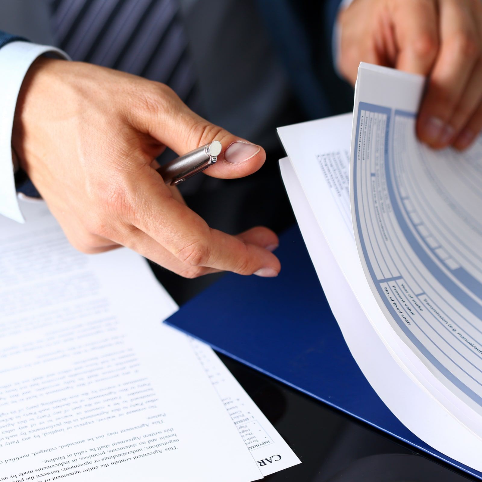 Male arm in suit offer insurance form clipped to pad and silver pen to sign closeup