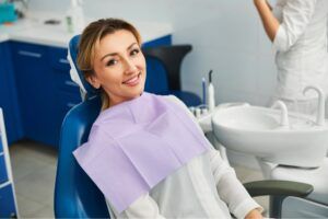 Woman in a dental office having a seat in a medical chair with cloth on her chest and smiling